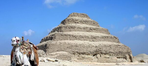 A photo showing the stepped pyramid of Djoser at Saqqara in Egypt, with a camel in the foreground.