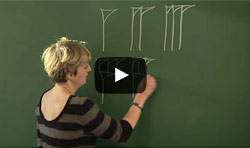 woman writing Sumarian numbers on a blackboard