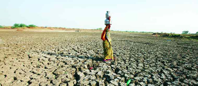 Woman carrying water on her head over parched land 