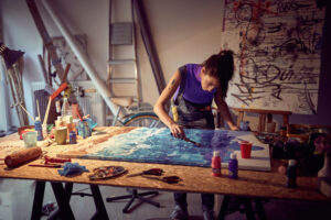 A female artist painting on a table in a studio.