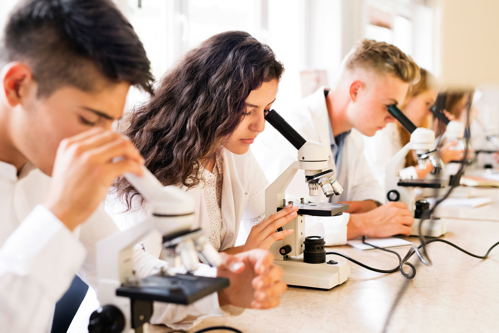 A group of high school students in a science lab looking through microscopes.