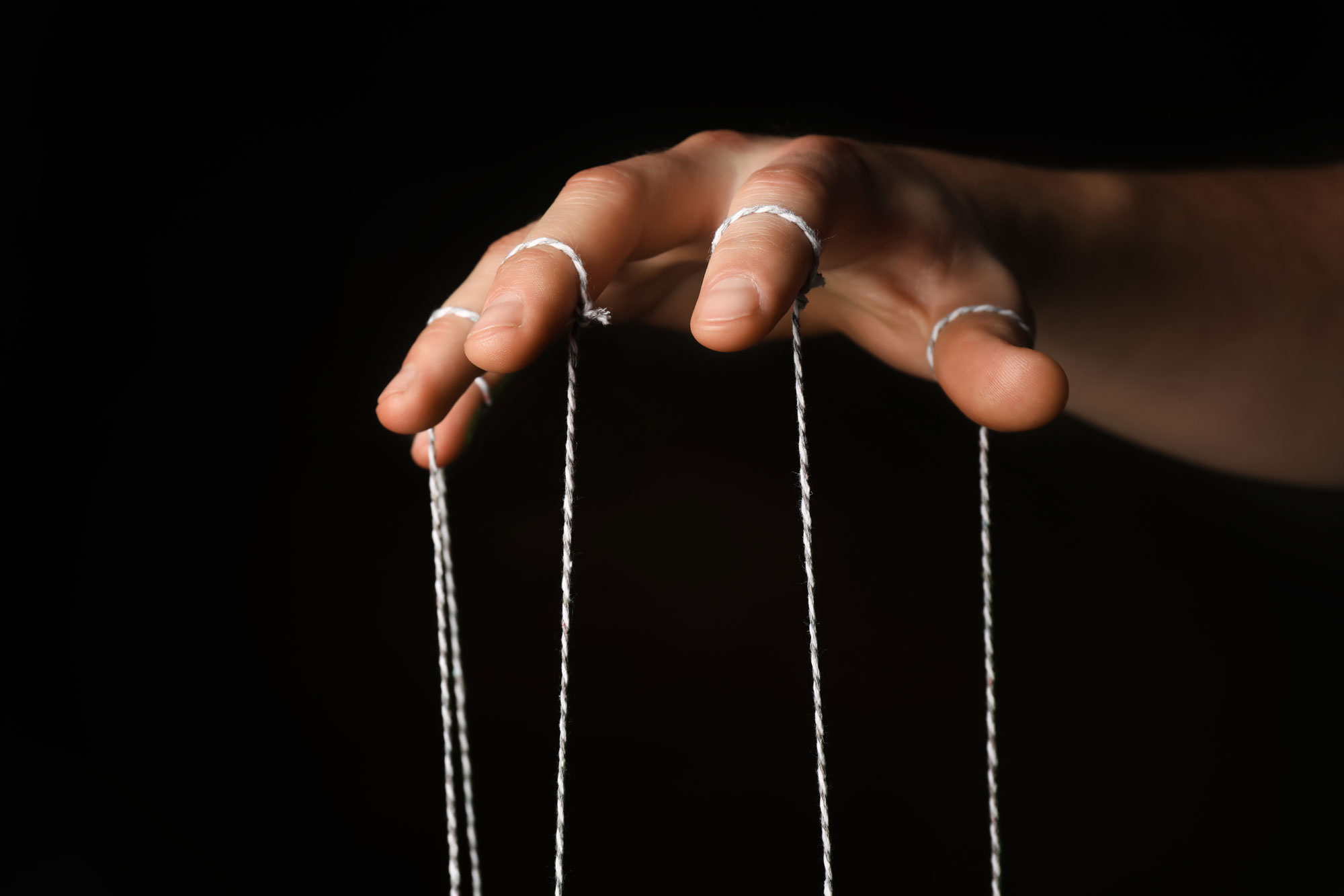 A person's hand with strings manipulating a hidden puppet below the image.