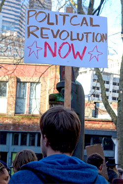 A political protester holding up a sign that reads 'Political Revolution Now'.