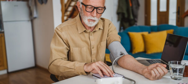 A photo of a senior citizen testing his blood pressure with a a machine at home.