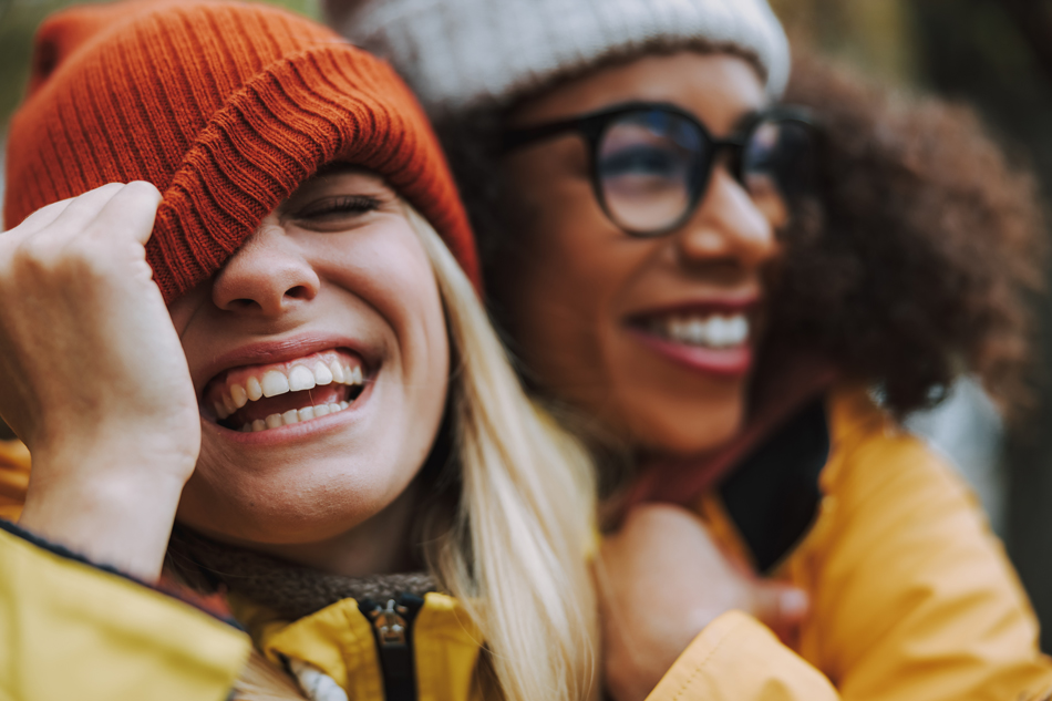 Two women hugging and laughing in a park, communicating in a friendly and intimate way.